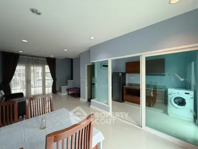 Modern open-plan living room with dining area and glass-enclosed kitchen featuring a washing machine.