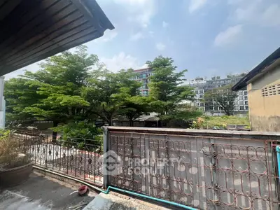 Charming balcony view with lush greenery and modern buildings in the background.