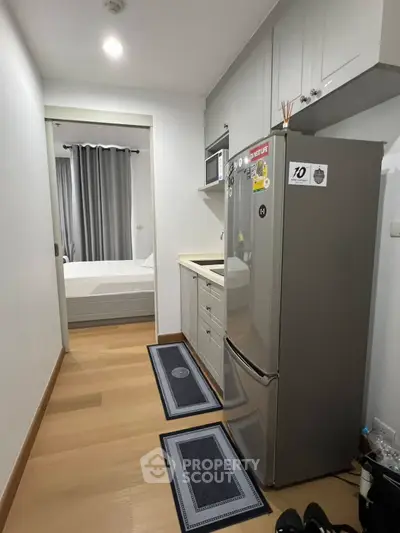 Compact kitchen with modern appliances leading to a cozy bedroom in a stylish apartment.