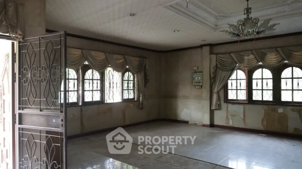 Spacious living room with elegant drapery and chandelier, featuring large windows and tiled flooring.