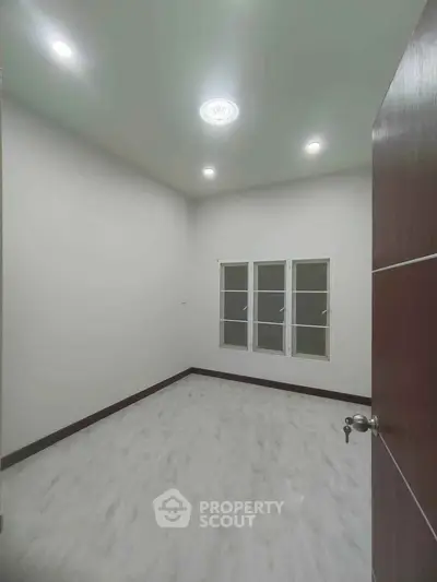 Spacious empty room with modern lighting and large window, perfect for customization.