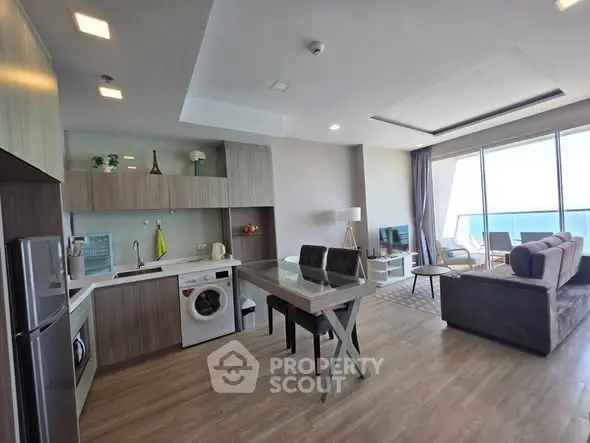 Modern open-plan living room and kitchen with ocean view, featuring sleek furniture and natural light.