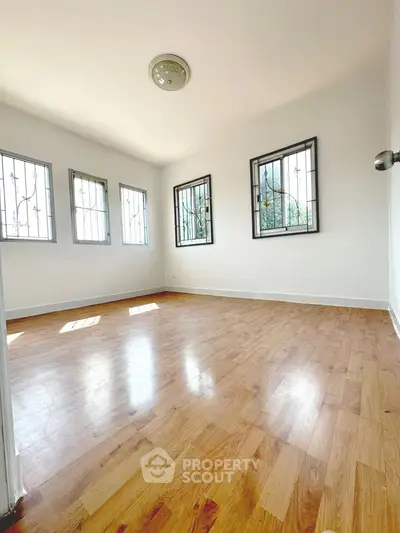 Spacious sunlit room with hardwood floors and large windows, perfect for a cozy living area.