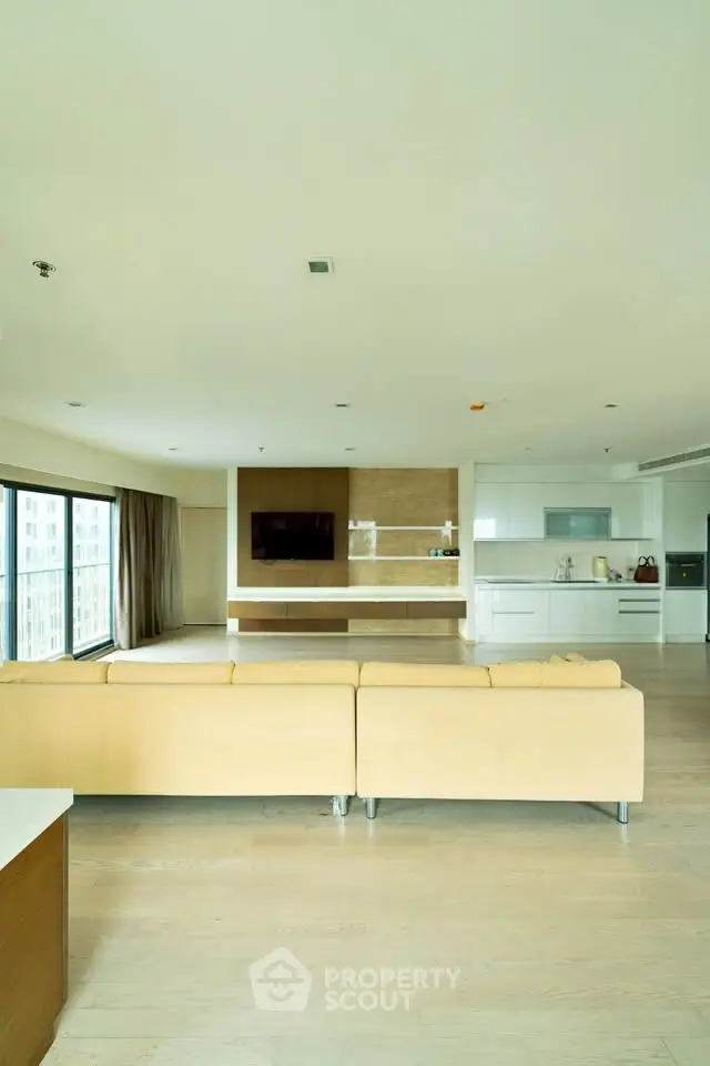 Spacious modern living room with open kitchen and large windows offering city views.
