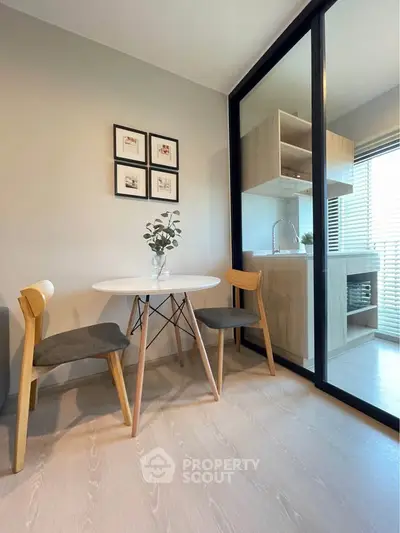 Modern dining area with sleek table and chairs, adjacent to a compact kitchen with glass partition.