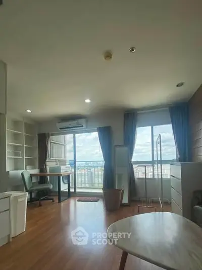 Spacious living room with large windows offering stunning city views, featuring modern furniture and wooden flooring.