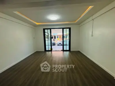 Spacious living room with wooden flooring and large glass doors leading to a bright exterior view.