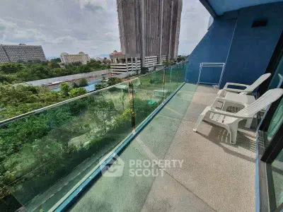 Spacious balcony with glass railing offering stunning city views and outdoor seating.
