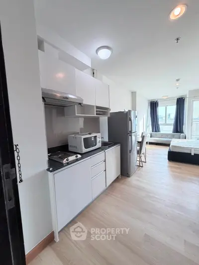 Modern studio apartment with open kitchen and bright living area, featuring sleek appliances and large windows.