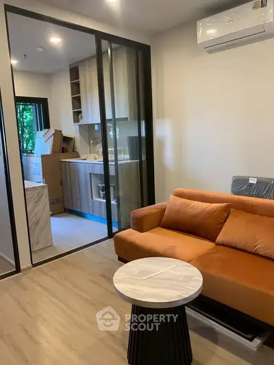 Modern living room with orange sofa and open kitchen layout, featuring sleek cabinetry and air conditioning.