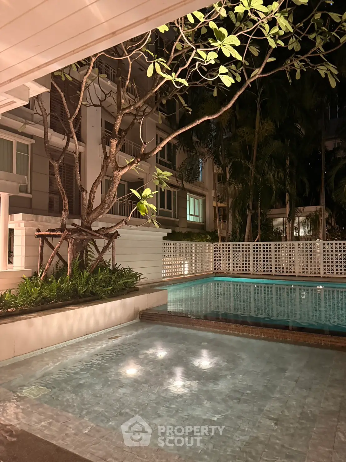 Luxurious night view of a serene residential pool surrounded by lush greenery and modern architecture.