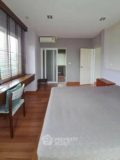 Spacious bedroom with wooden flooring and large window for natural light.