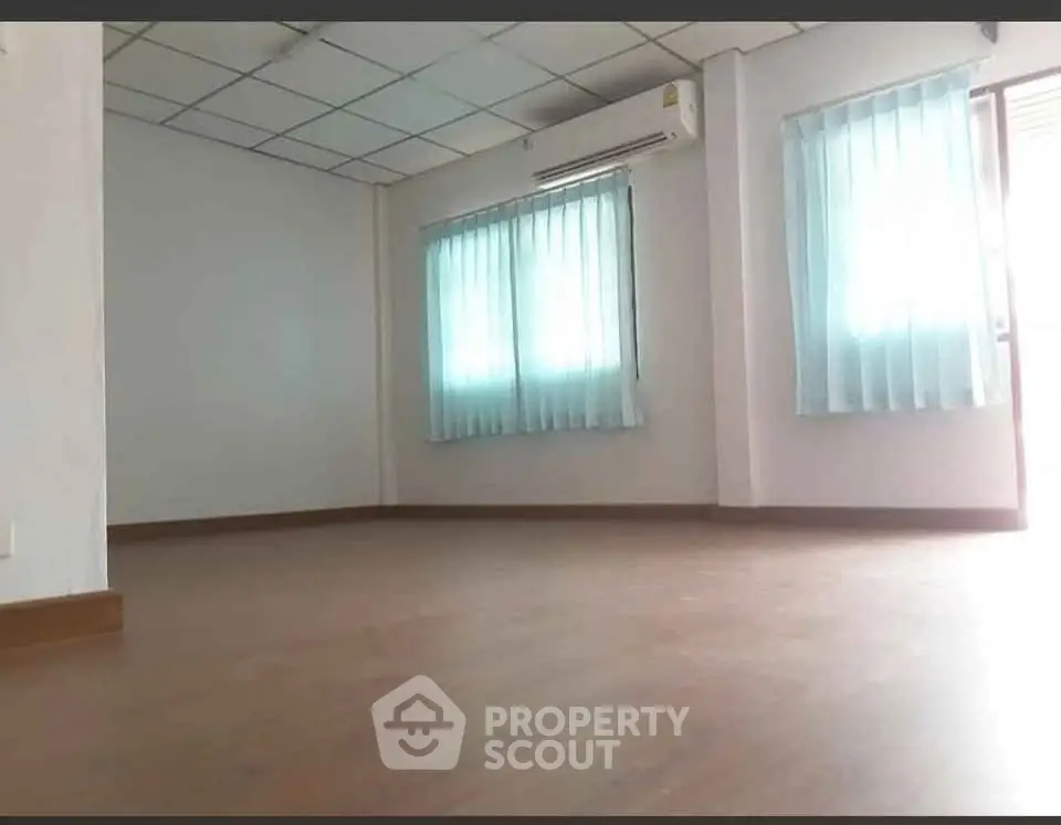 Spacious empty room with wooden flooring and large windows, perfect for customization.