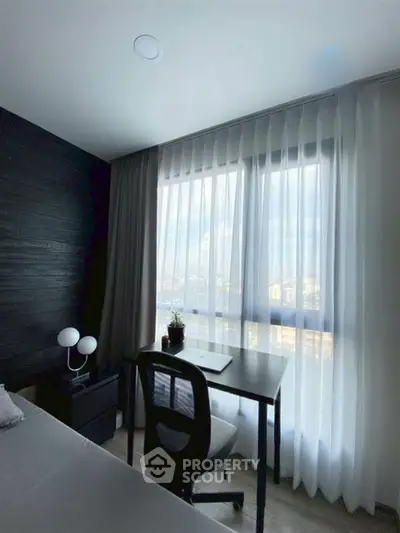 Modern bedroom with sleek desk and city view through large window.