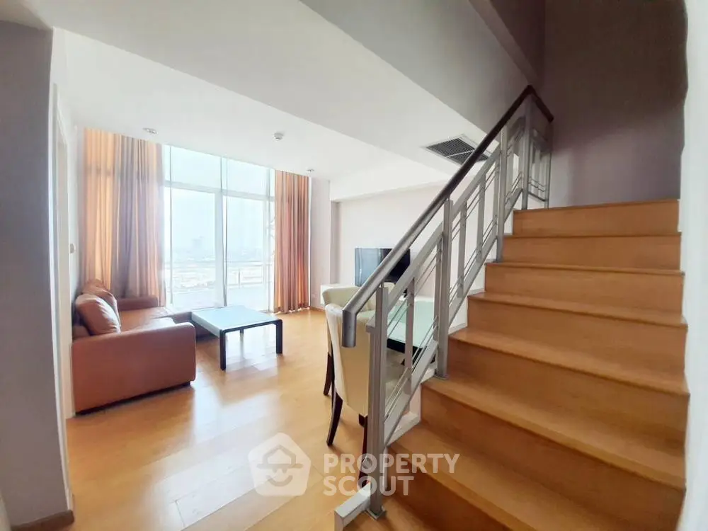 Spacious living room with modern staircase and large windows offering city views.