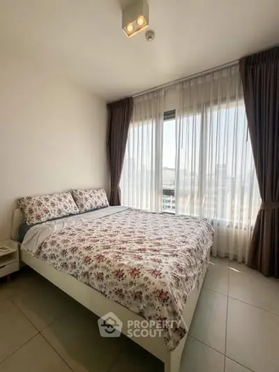 Bright bedroom with floral bedding and large window offering city views.