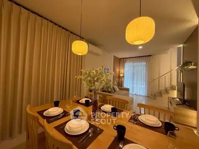 Elegant dining area with wooden table, stylish lighting, and cozy living room in modern home.