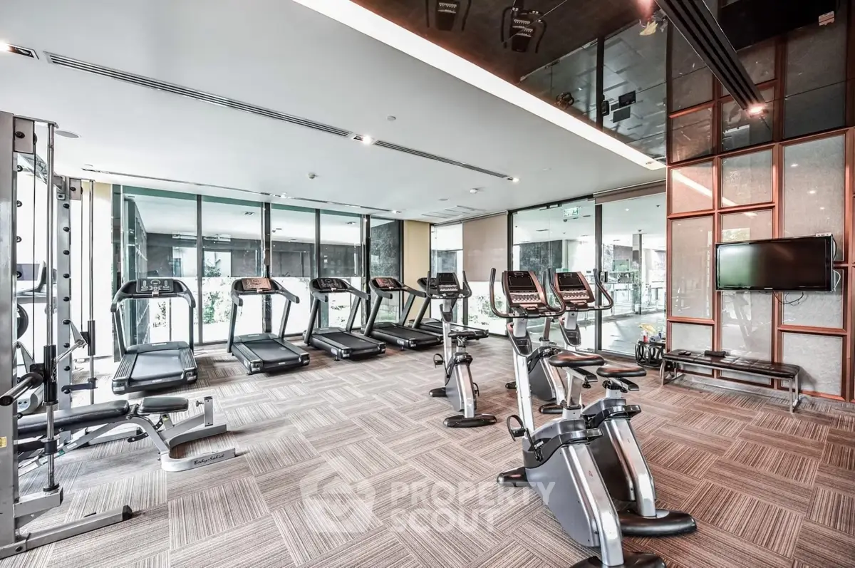 Modern gym with state-of-the-art equipment and floor-to-ceiling windows in luxury apartment building.