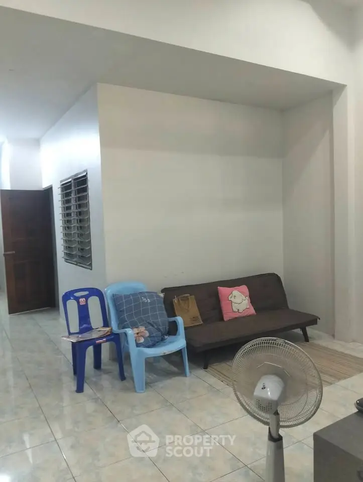 Cozy living room with minimalist decor and tiled flooring, featuring a sofa and fan for comfort.