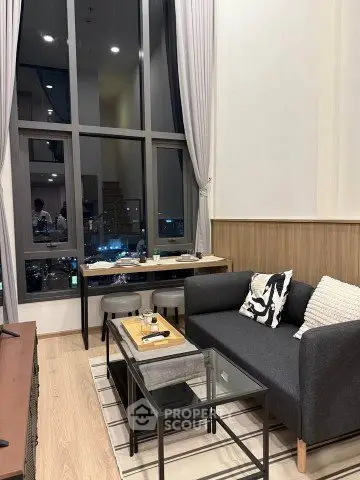 Modern living room with high ceilings and large windows offering city views.
