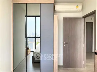 Modern bedroom with mirrored wardrobe and city view, featuring sleek air conditioning unit.
