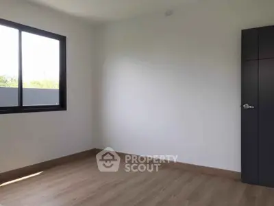 Spacious empty bedroom with large window and wooden flooring
