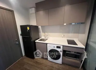 Modern compact kitchen with appliances including washing machine and fridge, sleek cabinetry, and wood flooring.