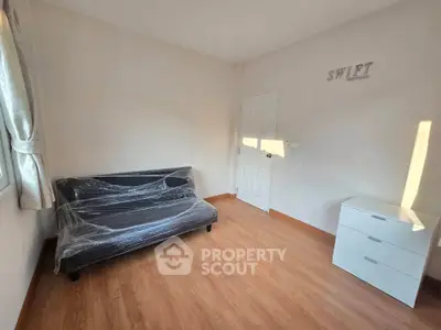 Minimalist room with a wrapped sofa and dresser, featuring wooden flooring and natural light.