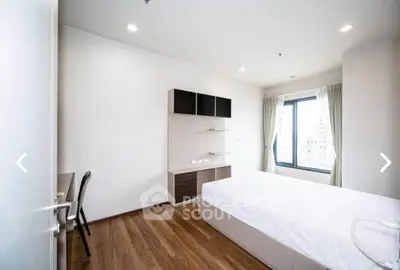 Modern minimalist bedroom with wooden flooring and large window offering city views.
