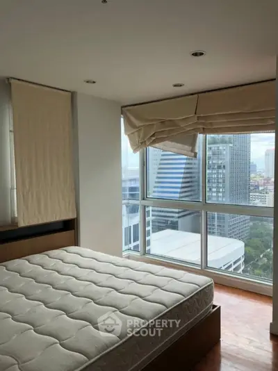 Modern bedroom with large windows offering stunning city views in a high-rise apartment.