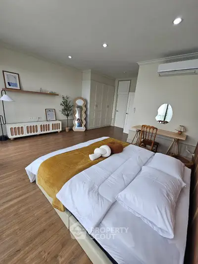 Spacious bedroom with modern decor and wooden flooring, featuring a cozy bed and stylish furniture.