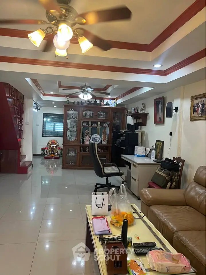 Spacious living room with modern decor and ceiling fan, featuring a cozy seating area and elegant display cabinet.
