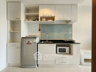 Modern kitchen with sleek white cabinets, compact fridge, and built-in microwave in a stylish apartment.