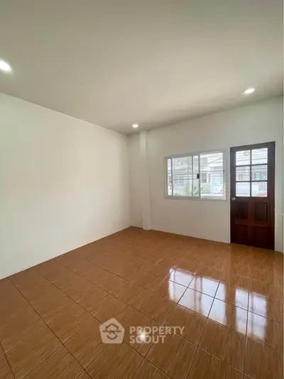 Spacious empty room with tiled floor and natural light through window and door.