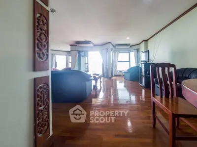 Spacious living room with wooden flooring and elegant decor, featuring a cozy seating area and large windows.