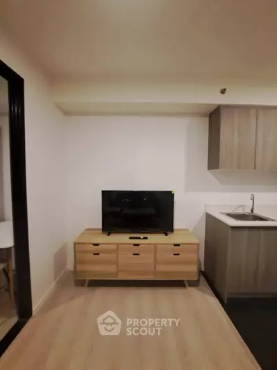 Modern living room with sleek TV stand and compact kitchenette in cozy apartment.