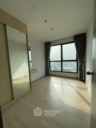 Bright bedroom with large window and wooden flooring offering city views.