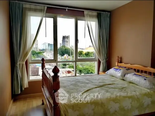 Cozy bedroom with large window offering stunning city views, featuring a wooden bed and elegant curtains.