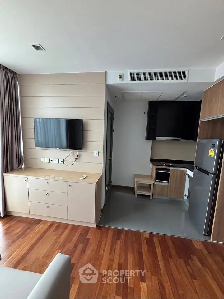 Modern living room with wooden flooring, wall-mounted TV, and compact kitchen area.