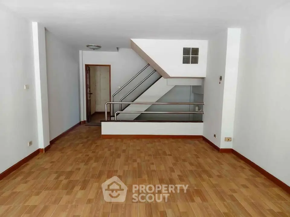 Spacious empty living room with wooden flooring and modern staircase, ideal for customization.