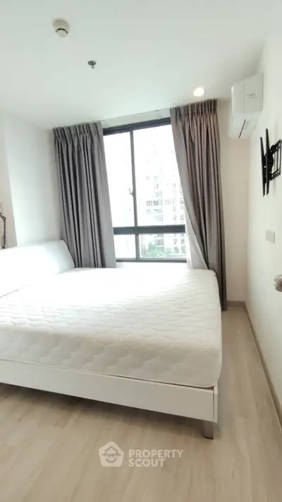 Modern bedroom with large window and minimalist decor in urban apartment.