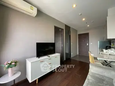 Modern living room with sleek furniture and open kitchen layout, featuring a TV and air conditioning.