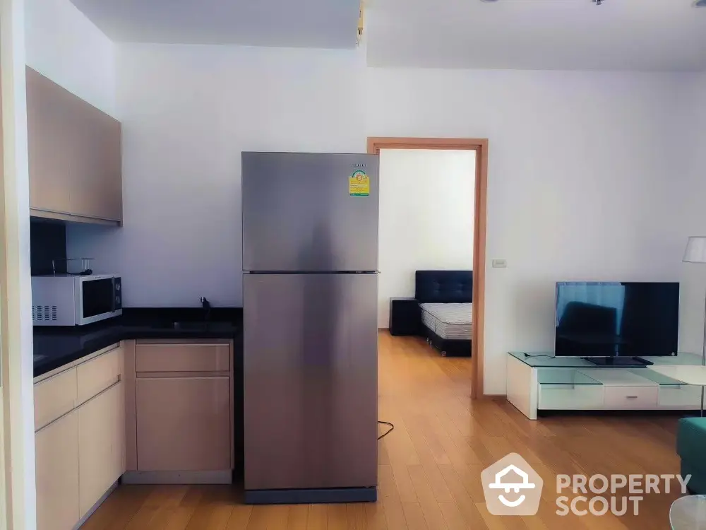 Modern apartment interior with kitchen and living area featuring sleek appliances and wooden flooring.