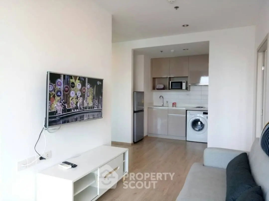 Modern living room with open kitchen, featuring a wall-mounted TV and sleek appliances.