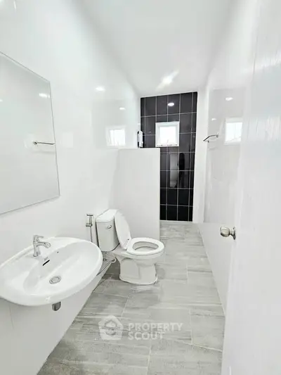 Modern bathroom with sleek design, featuring a white sink, toilet, and tiled shower area.