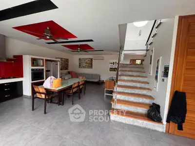 Modern open-plan living room with stylish red accents and sleek staircase