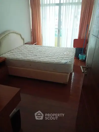 Cozy bedroom with natural light and wooden flooring, featuring a comfortable bed and elegant curtains.