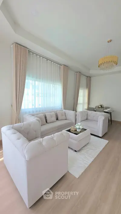 Elegant living room with plush sofas, chic chandelier, and dining area in modern open layout.