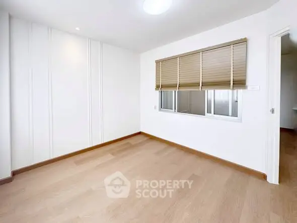 Spacious empty room with wooden flooring and window blinds, perfect for customization.