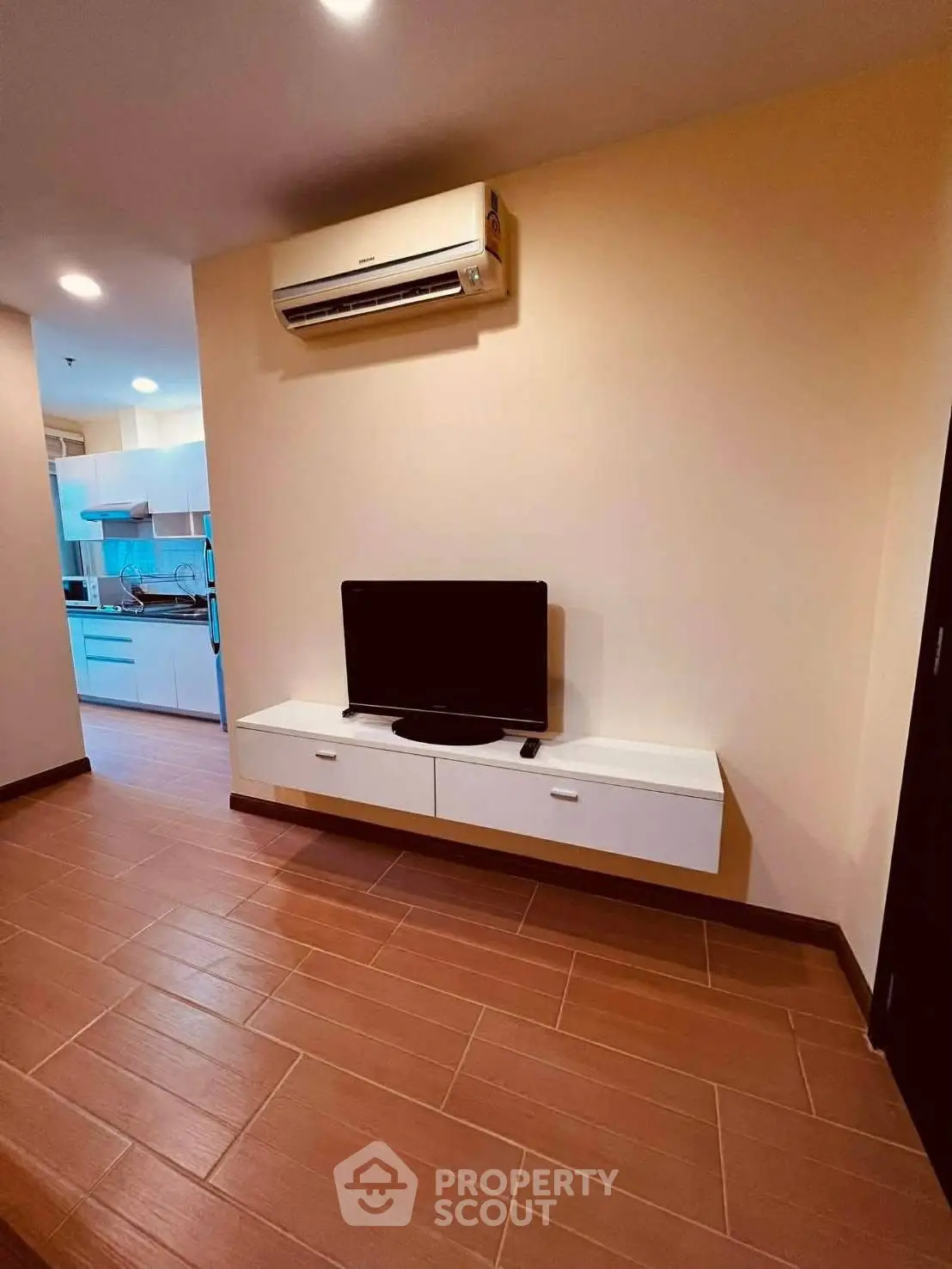 Modern living room with wall-mounted TV and air conditioning, leading to a sleek kitchen.
